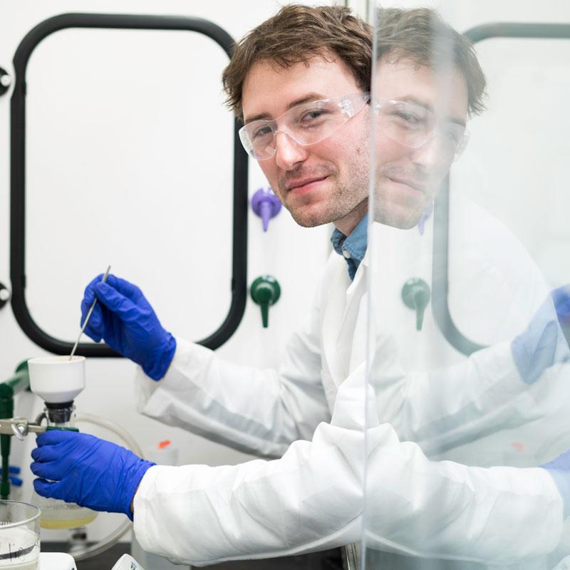 A researcher in a lab coat and gloves conducts experiments in the University of Rochester research lab.