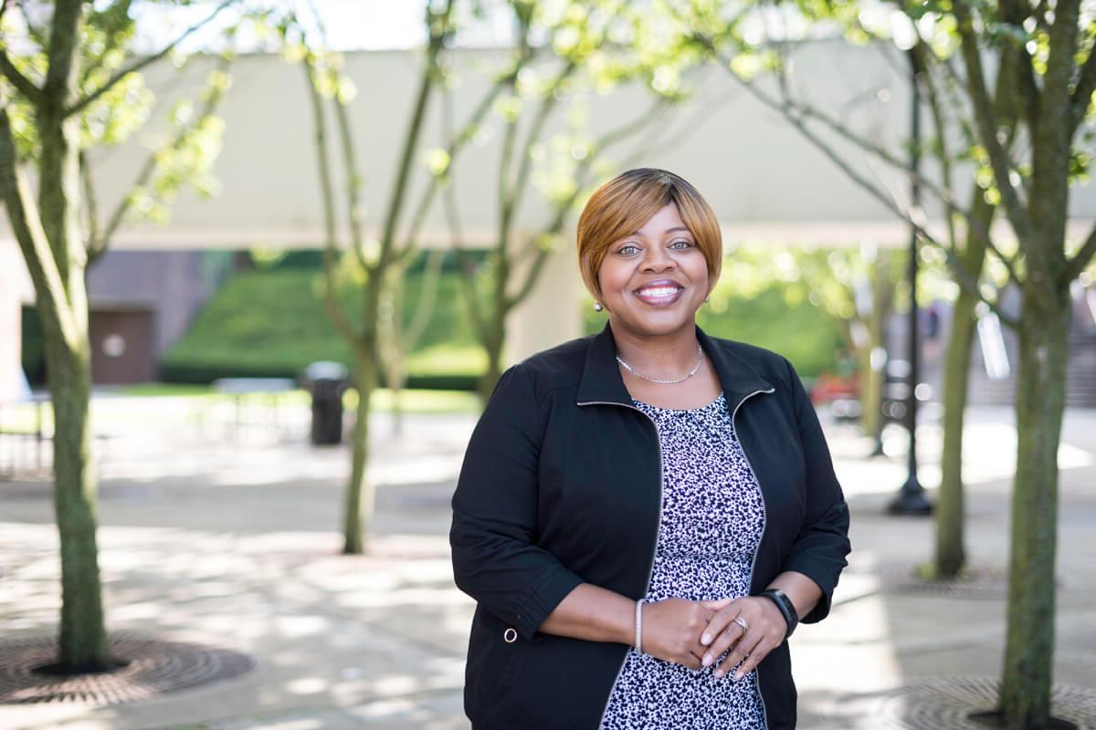 Dawn Bruner, a staff member at the University of Rochester, poses on campus with trees in the background.